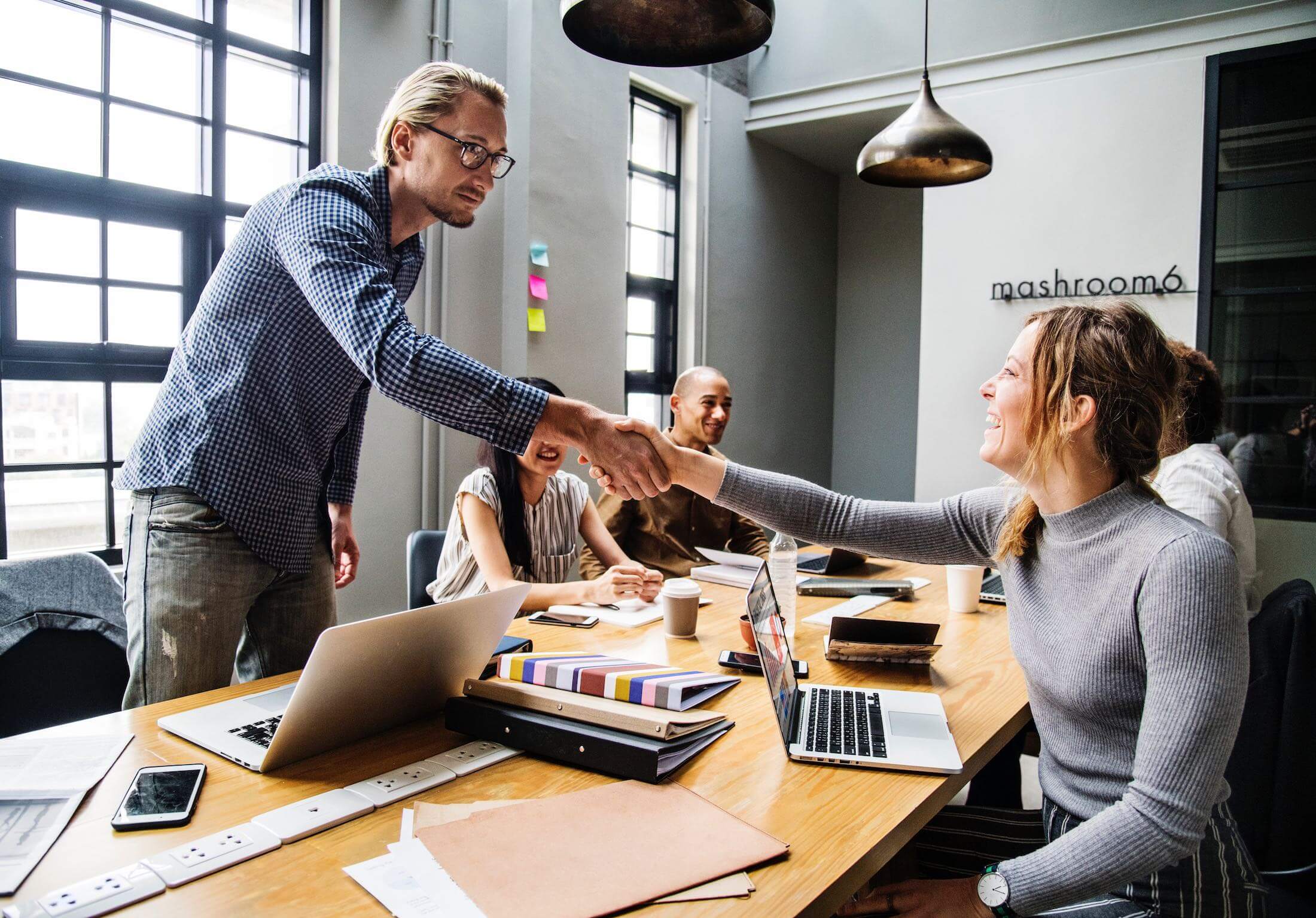 how-to-avoid-design-by-committee person standing and shaking the hand of other person sitting at a conference room table.
